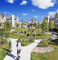 Children and adults representing a range of ages play and picnic in the common space of a community development