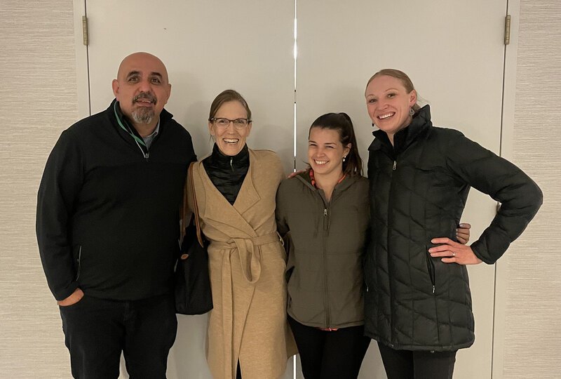 Four people pose in front of conference room doors