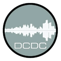 Circular logo with a gray background featuring a white silhouette of a city skyline mirrored vertically, resembling a soundwave, and the letters ‘DCDC’ below.